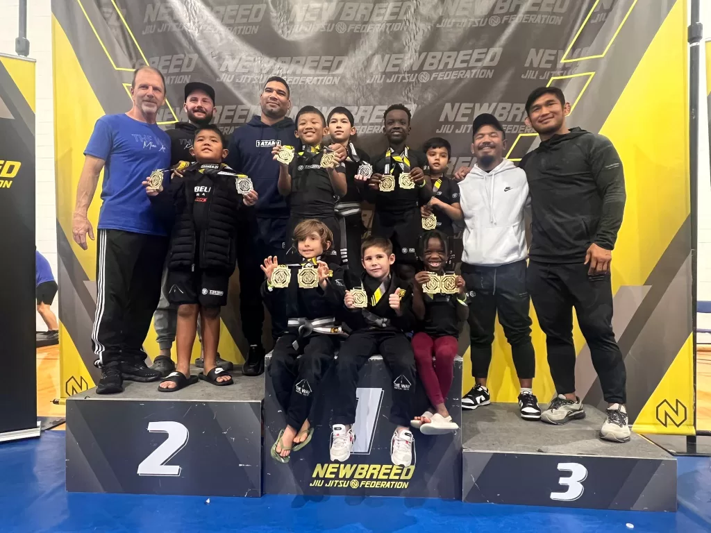 Young athletes from The Way Martial Arts in Lantana, Florida, celebrate their victories at the Newbreed Jiu-Jitsu Federation competition. Coaches and kids proudly display their medals on the podium, highlighting their dedication, hard work, and the Unbreakable Warrior Spirit. BJJ kids competition success in Florida.